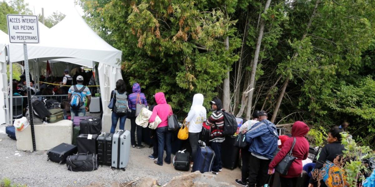 Una fila de solicitantes de asilo que decían ser de Haití aguardan para entrar a Canadá desde Roxham Road en Champlain, Nueva York, Aug. 7, 2017.